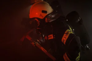 Strażak w hełmie i masce tlenowej pracujący w gęstym dymie podczas akcji gaśniczej.